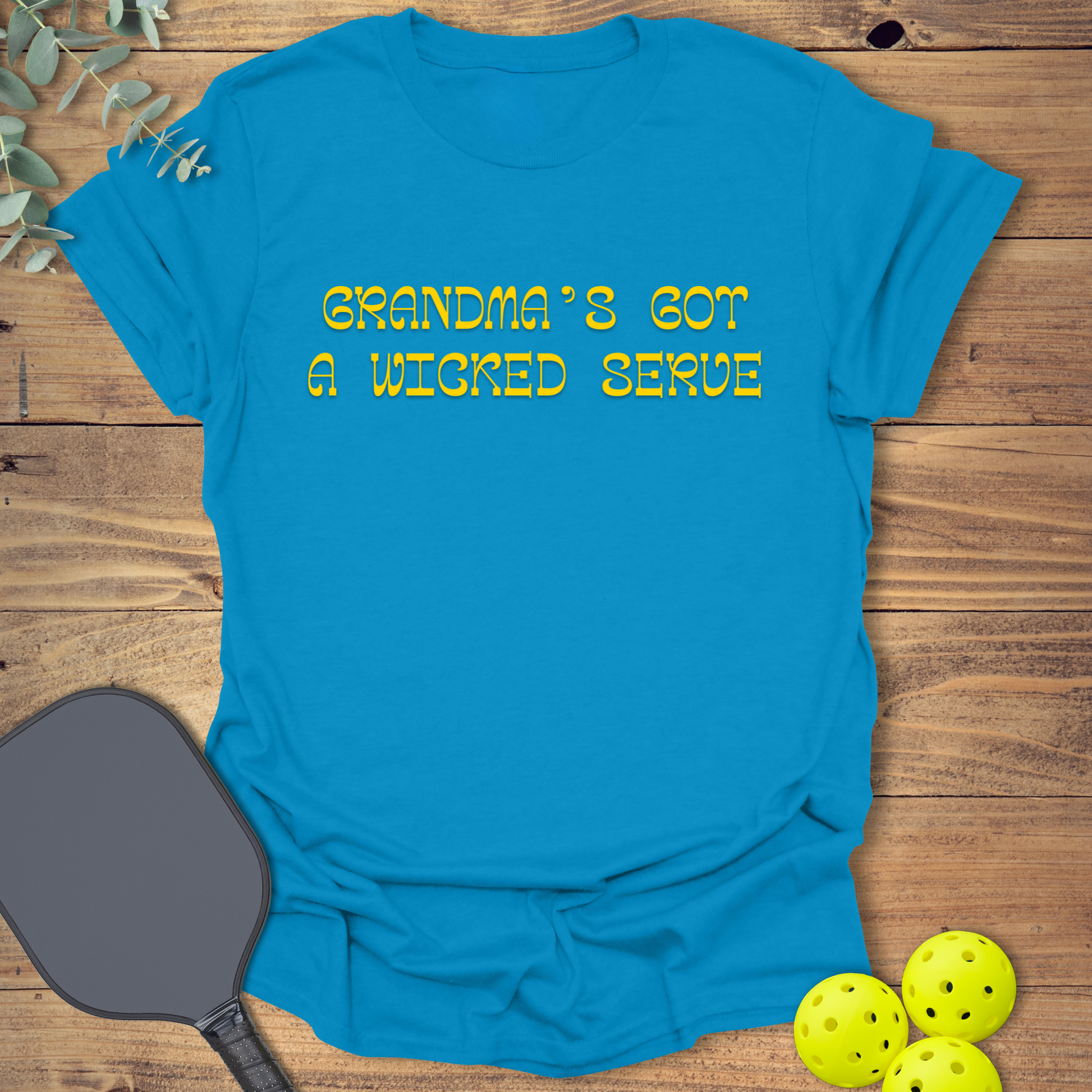 Blue pickleball t-shirt with “Grandma’s Got a Wicked Serve” printed in gold. Funny pickleball shirt for grandmas who play the game and serve with style.
