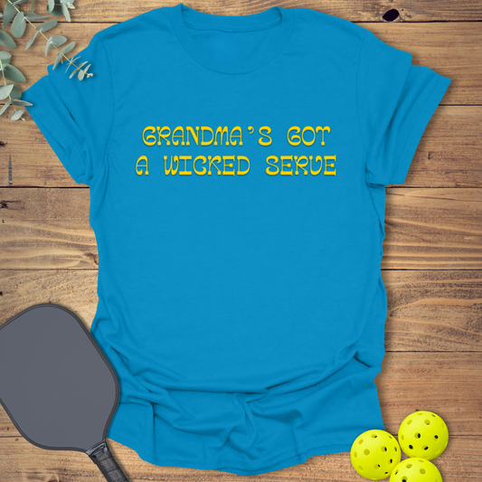 Blue pickleball t-shirt with “Grandma’s Got a Wicked Serve” printed in gold. Funny pickleball shirt for grandmas who play the game and serve with style.