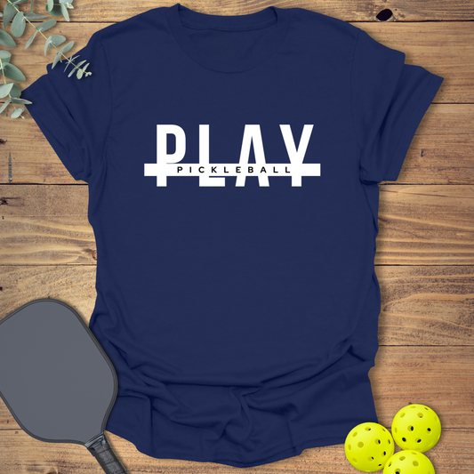 Navy blue graphic t-shirt with bold white text 'PLAY' split by a white horizontal bar, with smaller white text 'PICKLEBALL' centered on the bar