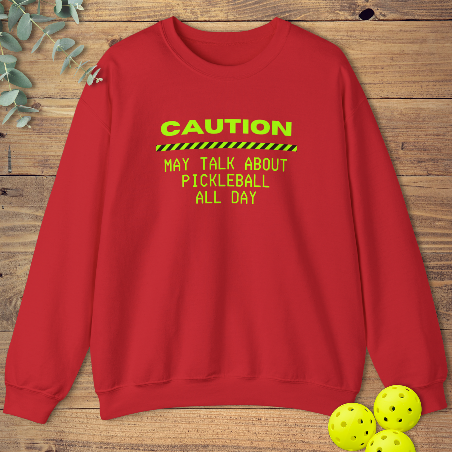 Red pickleball sweatshirt with neon green text that reads “Caution: May Talk About Pickleball All Day” and a caution stripe graphic.